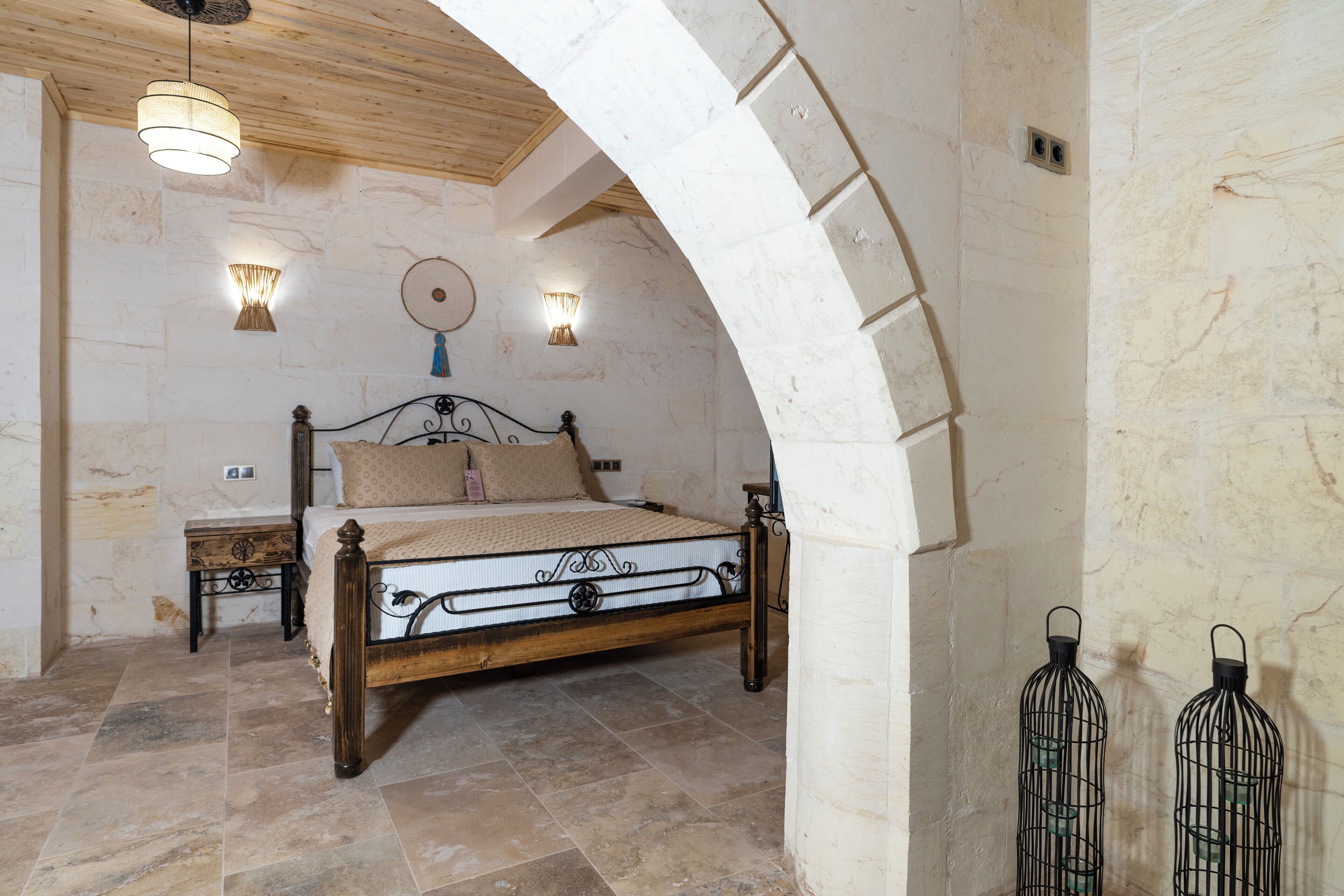 Une chambre à coucher avec un lit en bois, des murs en pierre et deux lampes fixées au mur.