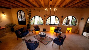 Un interior acogedor con vigas de madera, ventanas arqueadas y sillones tapizados en azul alrededor de una mesa de centro.
