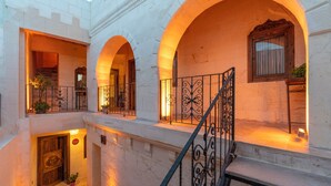 Un interior de varios niveles con balcones arqueados, una escalera y una puerta de madera.