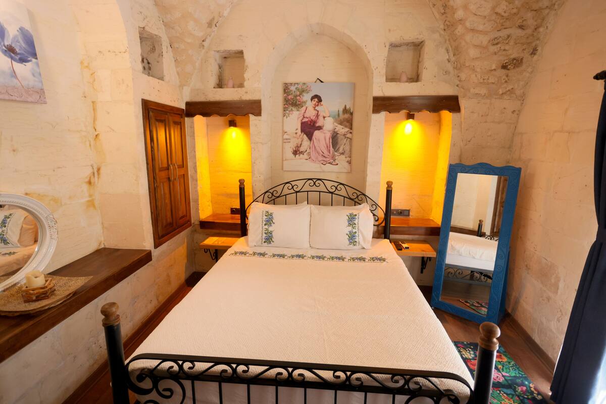 A bedroom with a bed, a wooden wardrobe, a mirror, and a painting on the wall.