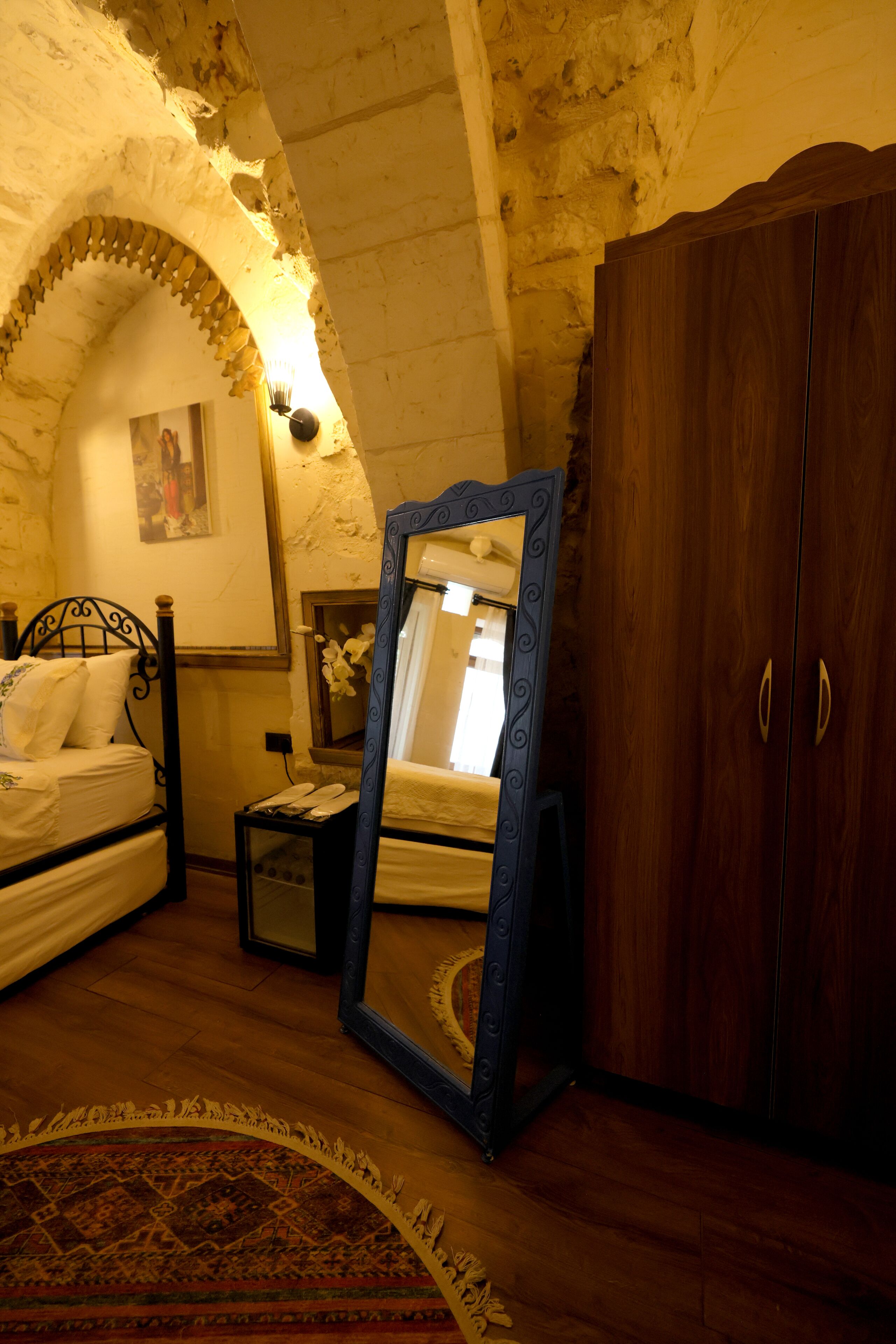 A bedroom with a bed, a wooden wardrobe, a mirror, and a small table with a telephone.