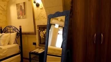 A bedroom with a bed, a wooden wardrobe, a mirror, and a small table with a telephone.
