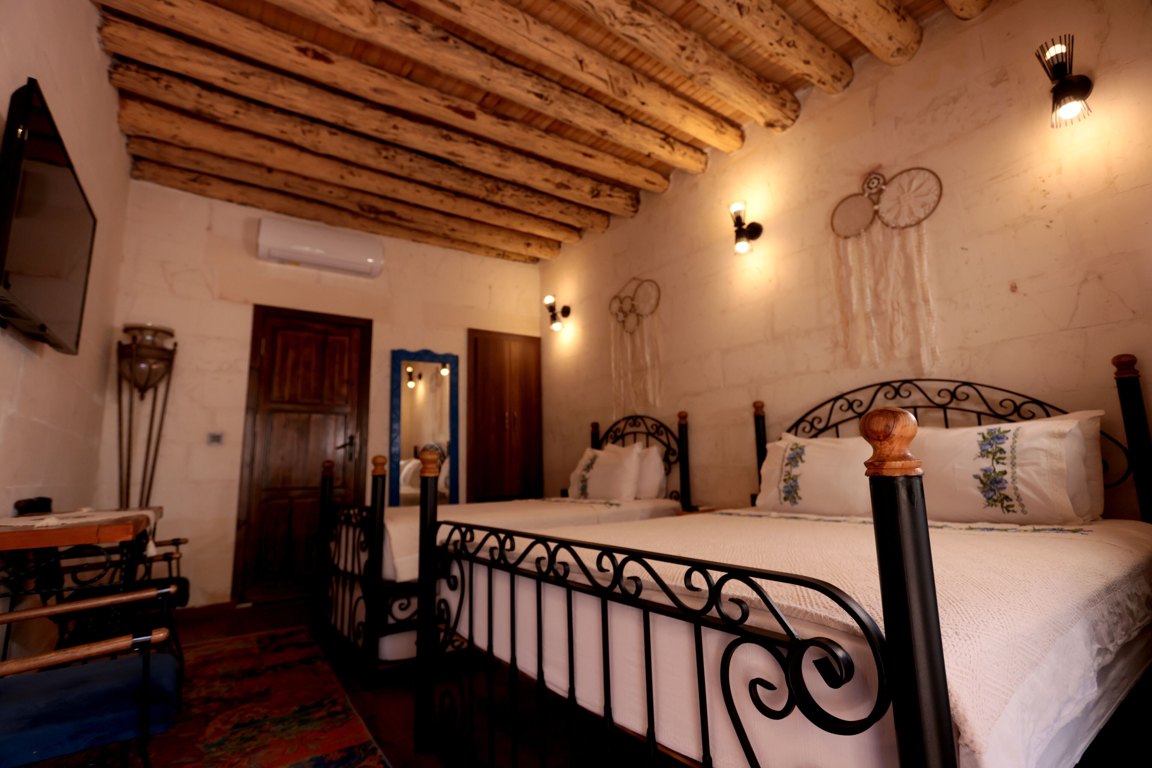 A bedroom with a wooden ceiling, a bed with a metal frame, a mirror, and wall-mounted lights.