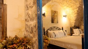 Un dormitorio con pared de piedra, suelo de madera, cama con ropa blanca y un espejo que refleja la habitación.