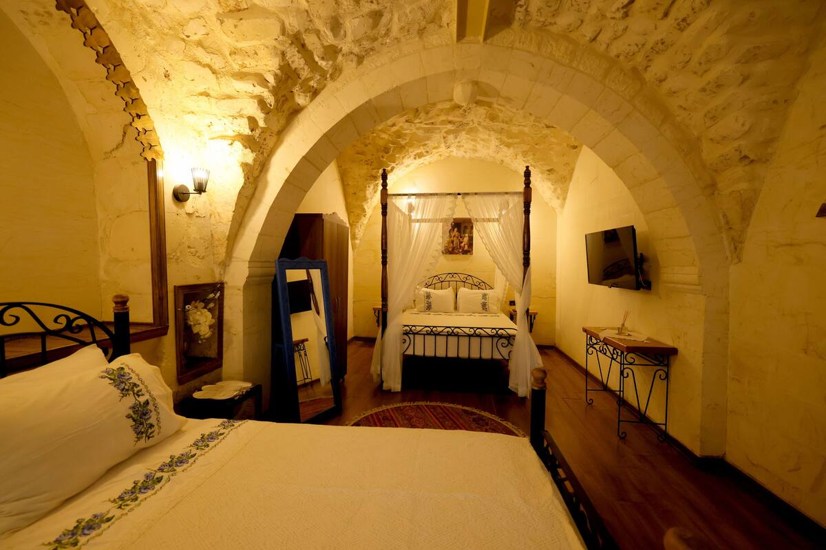 A bedroom with a four-poster bed, a wooden nightstand, a small table, and a TV mounted on the wall.
