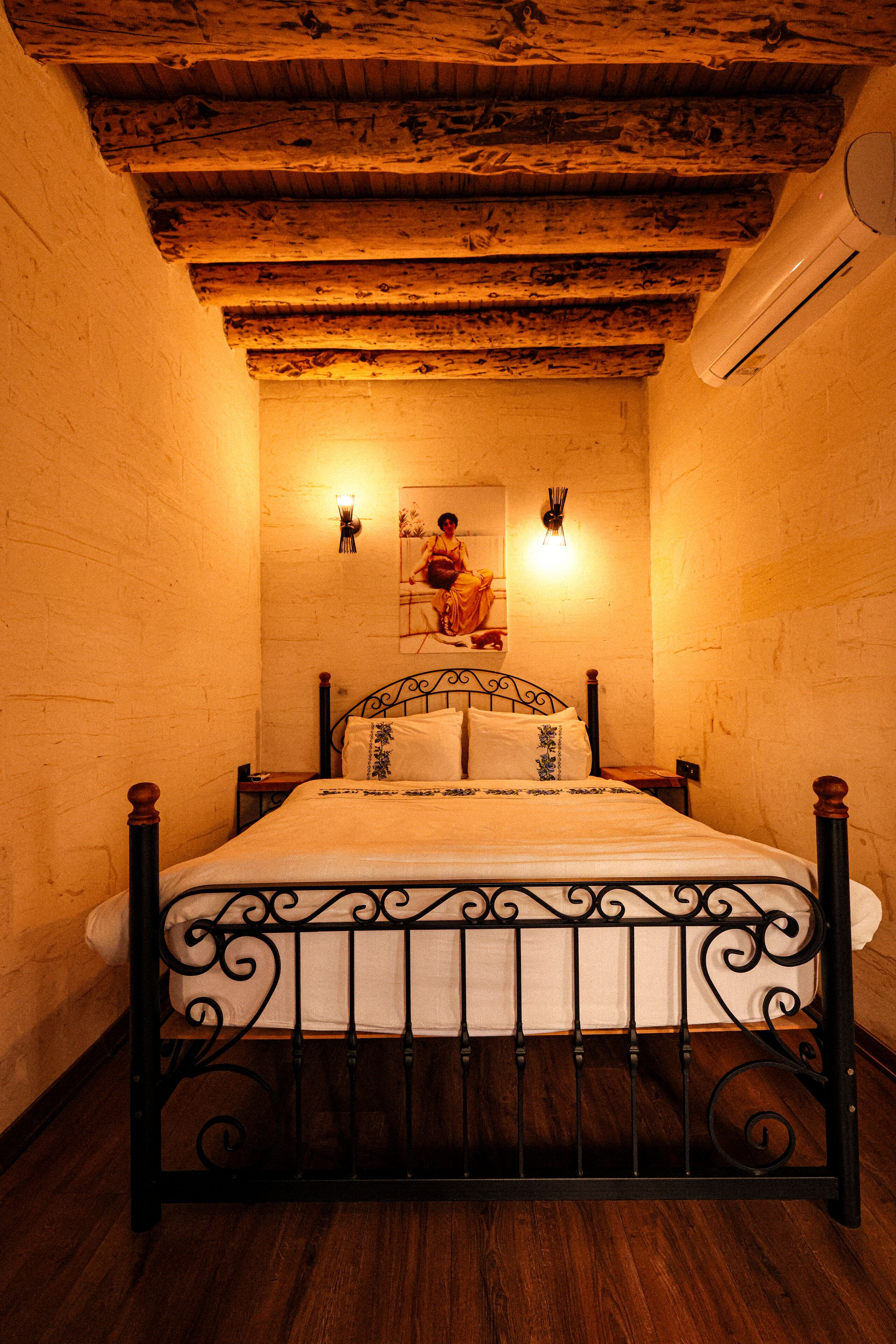 Un dormitorio con techo de madera, una cama con estructura metálica y dos luces fijadas a la pared.