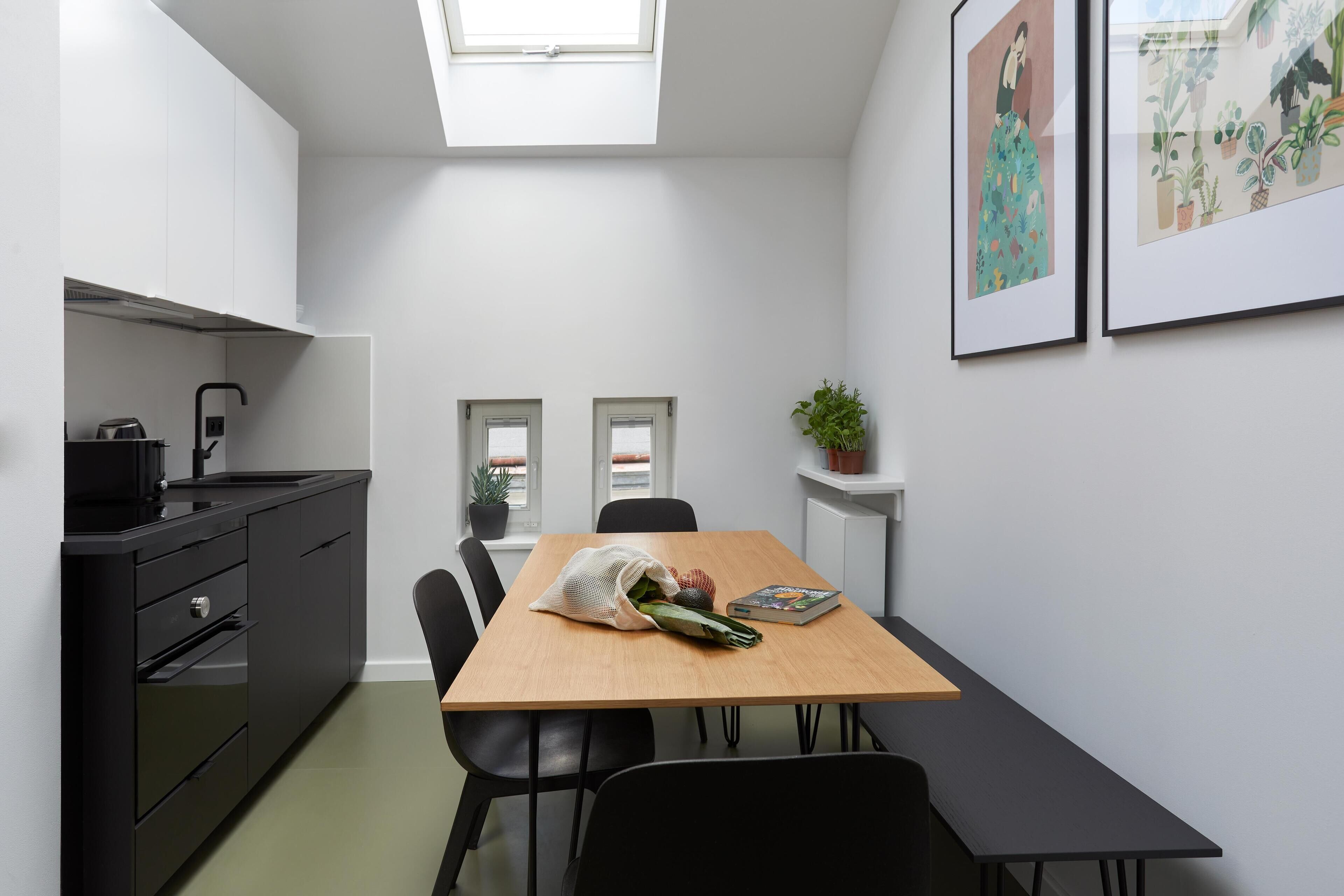 Une cuisine moderne avec un coin repas, comprenant une table en bois, des chaises noires, un plan de travail noir et une petite plante en pot.