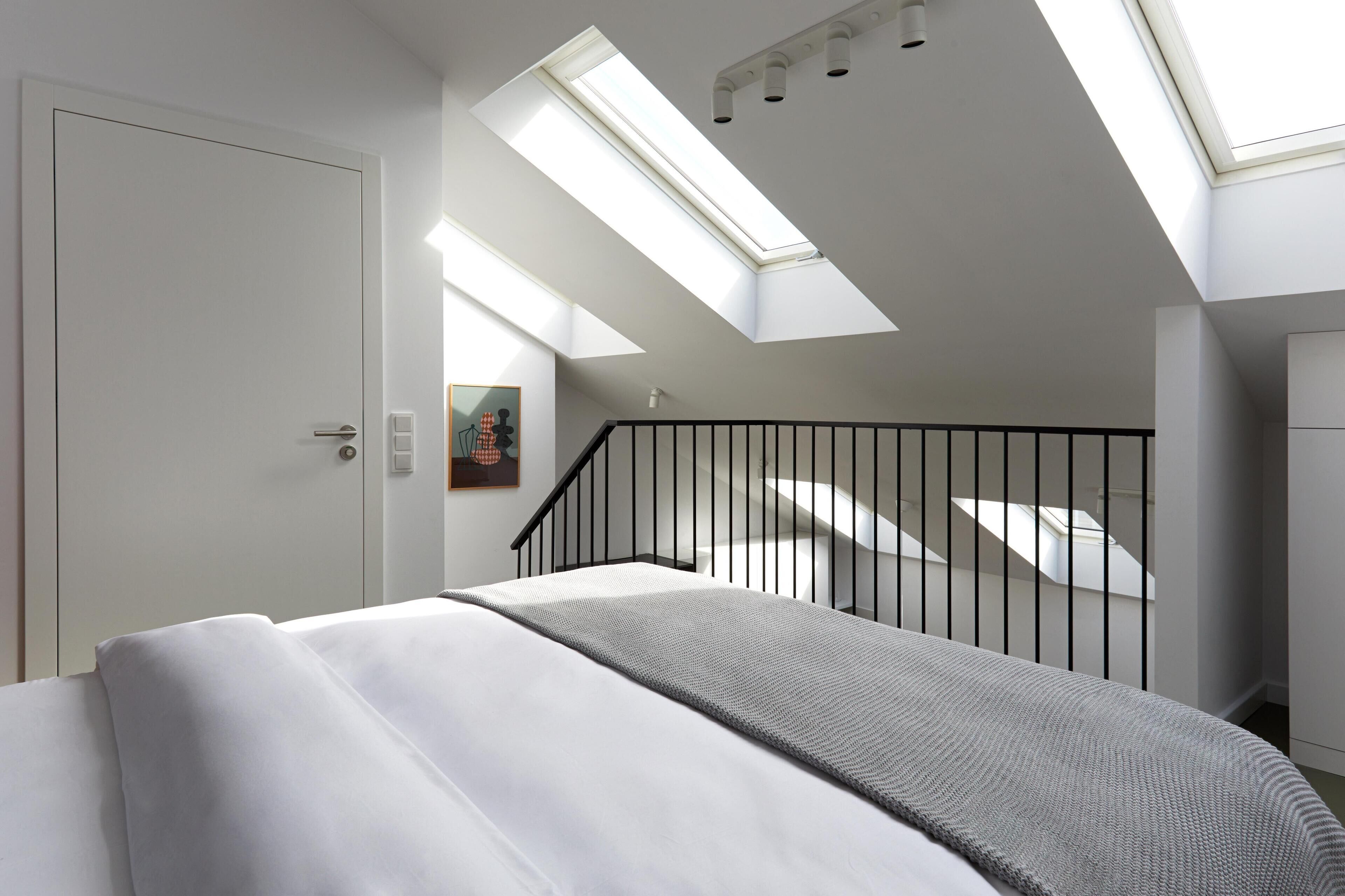 Un dormitorio moderno con tragaluces, una cama, una escalera y un cuadro en la pared.