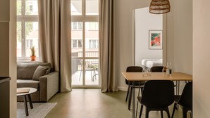 A modern living room with a sofa, a dining table with chairs, a hanging light fixture, and a view through a large window. - Plantonia (Kraków)