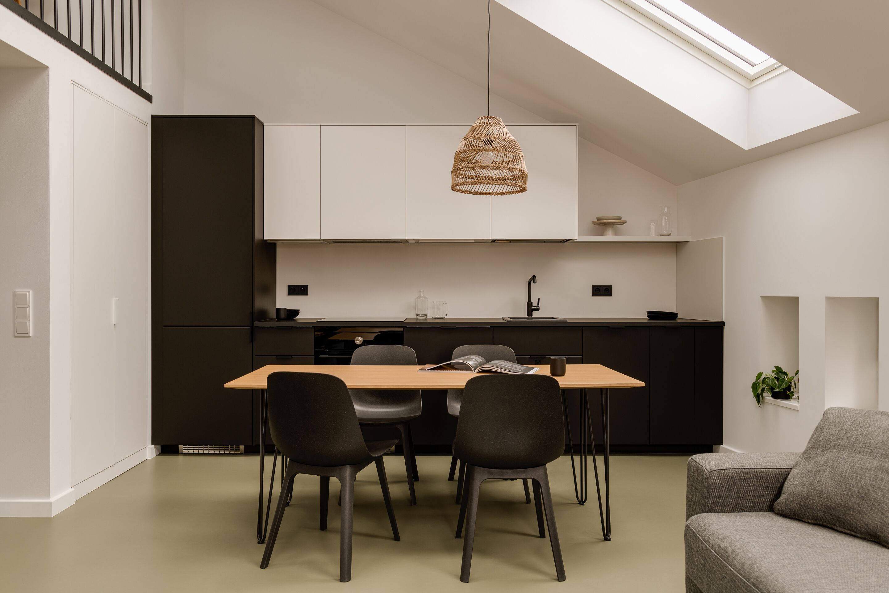 Een moderne keuken met een eethoek, met dakraam, zwarte kastjes en een houten tafel met stoelen.