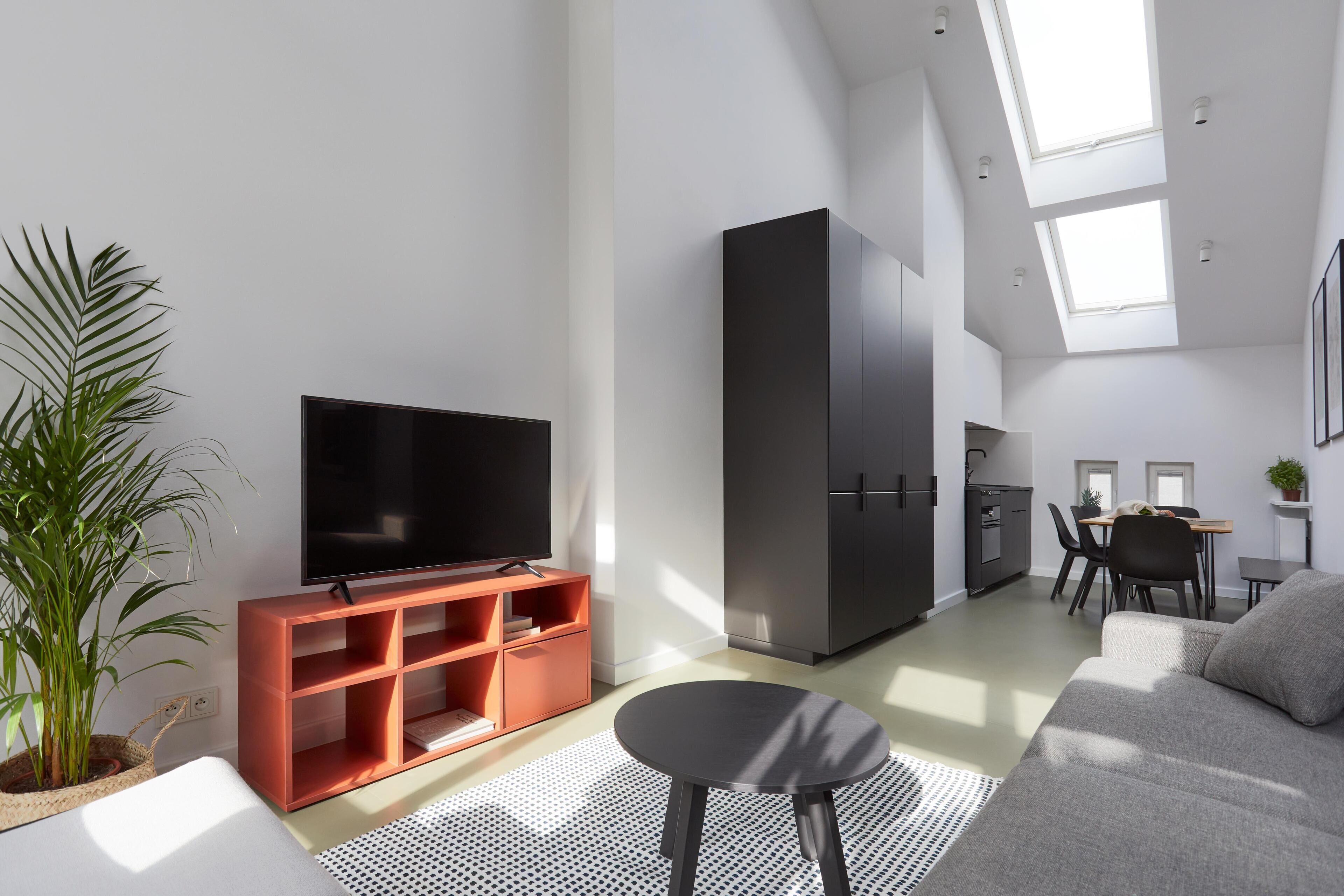 Una sala moderna con televisor de pantalla plana, un sofá, un comedor con mesa y sillas, y una cocina con armarios.