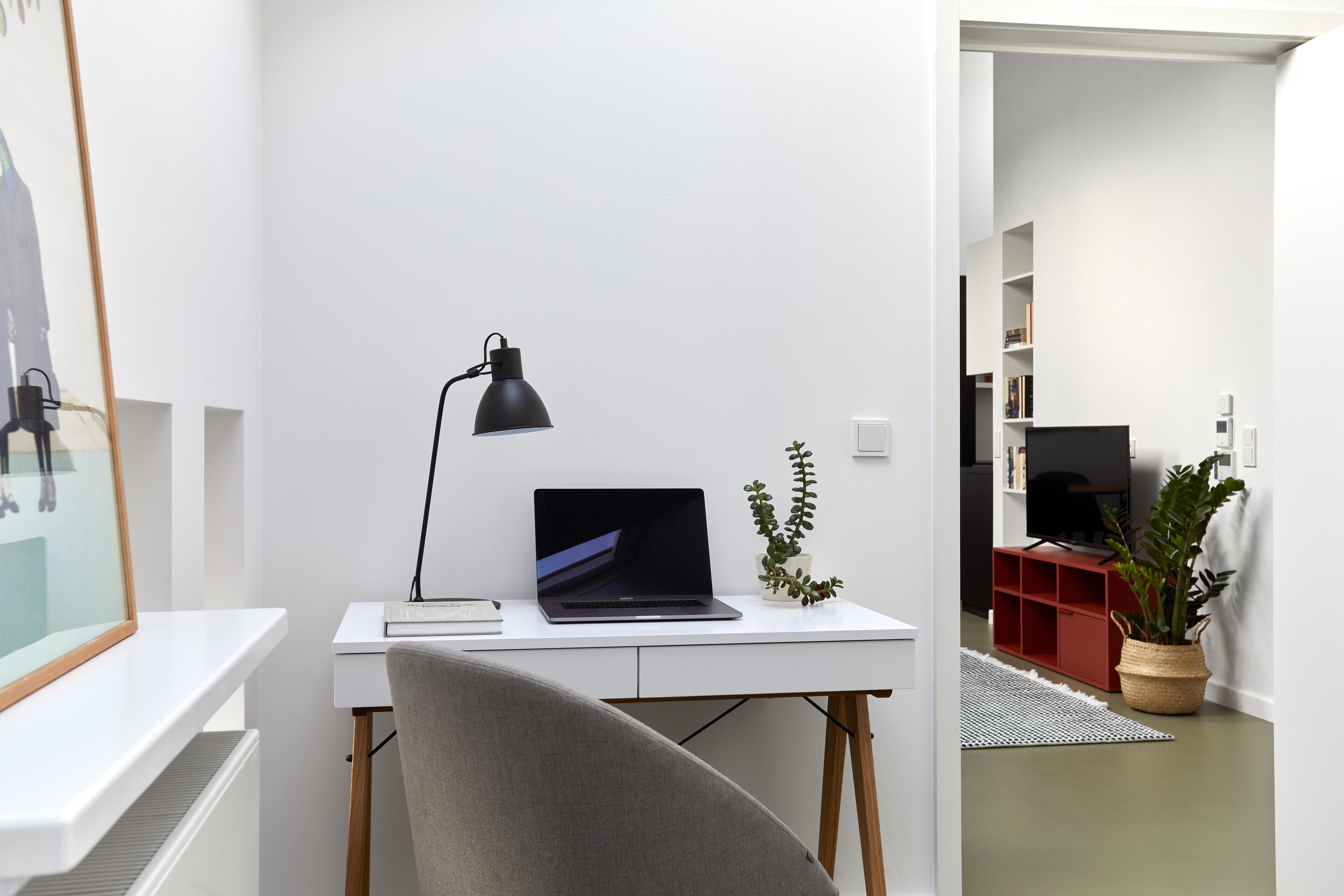 A modern, minimalist workspace with a laptop, a desk lamp, and a potted plant.