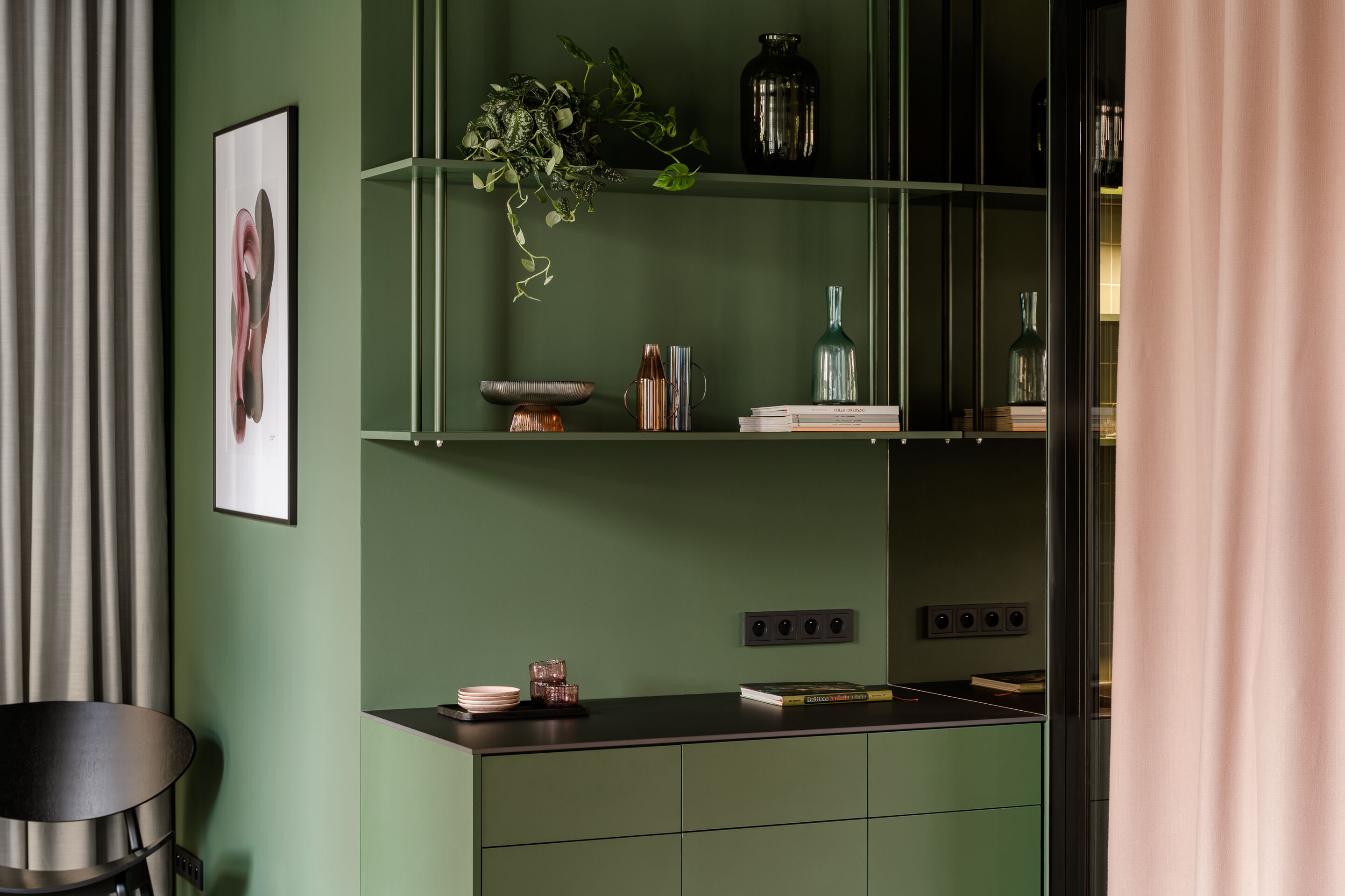 Une cuisine moderne avec des meubles de couleur verte, un plan de travail noir et une plante suspendue.