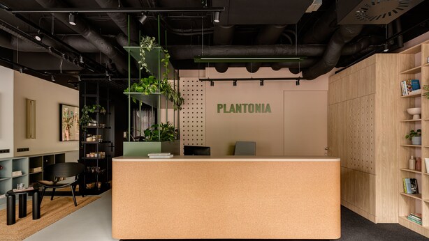 A reception desk with a 'PLANTONIA' sign, surrounded by shelves with books and plants, and a black chair. - Plantonia (Kraków)