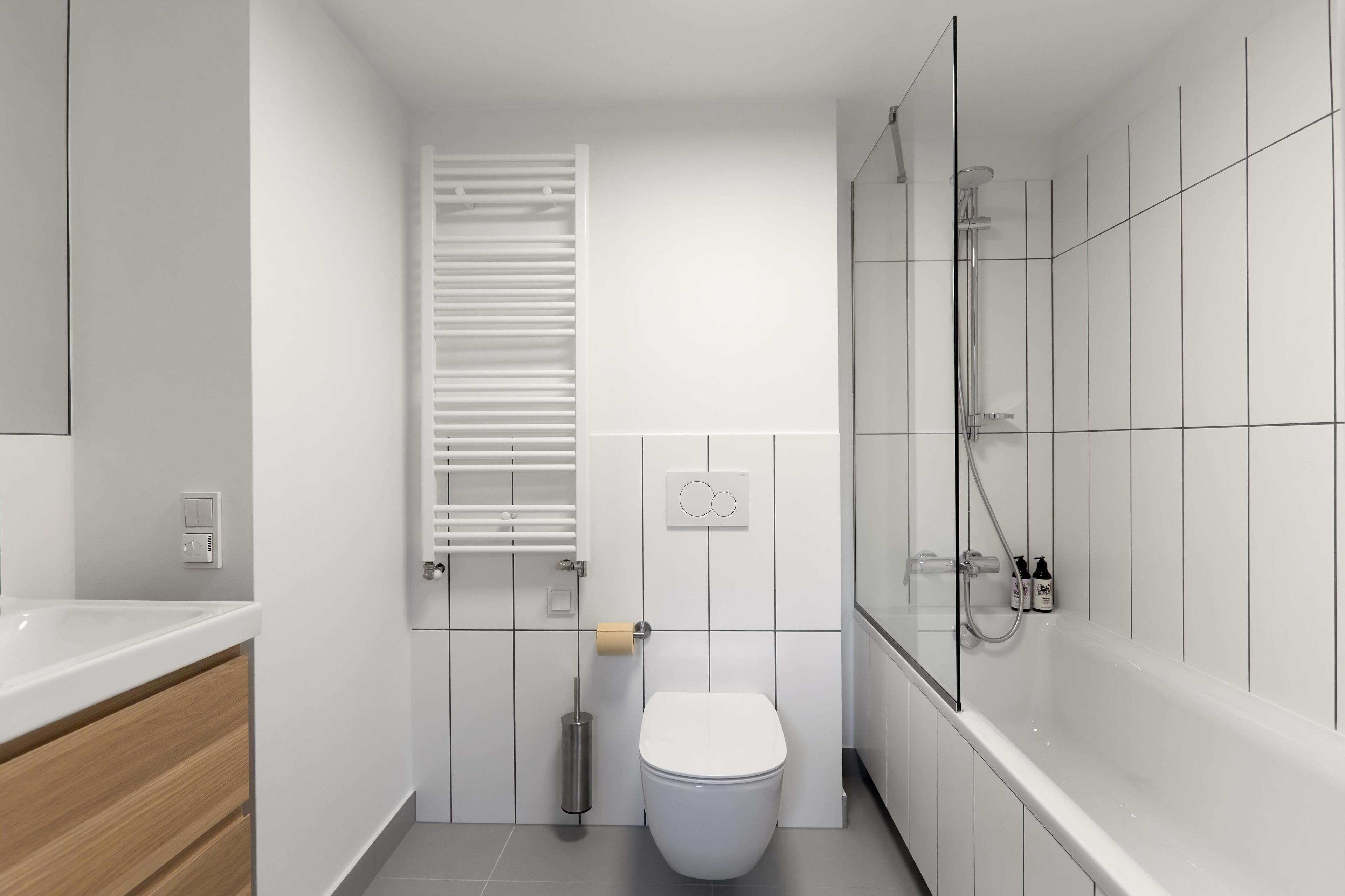Une salle de bain moderne avec des toilettes blanches, une douche dotée d’une paroi en verre et un meuble-lavabo en bois avec un lavabo blanc.