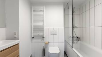 Un baño moderno con inodoro blanco, ducha con cabina de vidrio y tocador de madera con lavabo blanco.