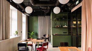 A modern office space with a wooden table, red and black chairs, a laptop, and a green wall with shelves. - Plantonia (Kraków)