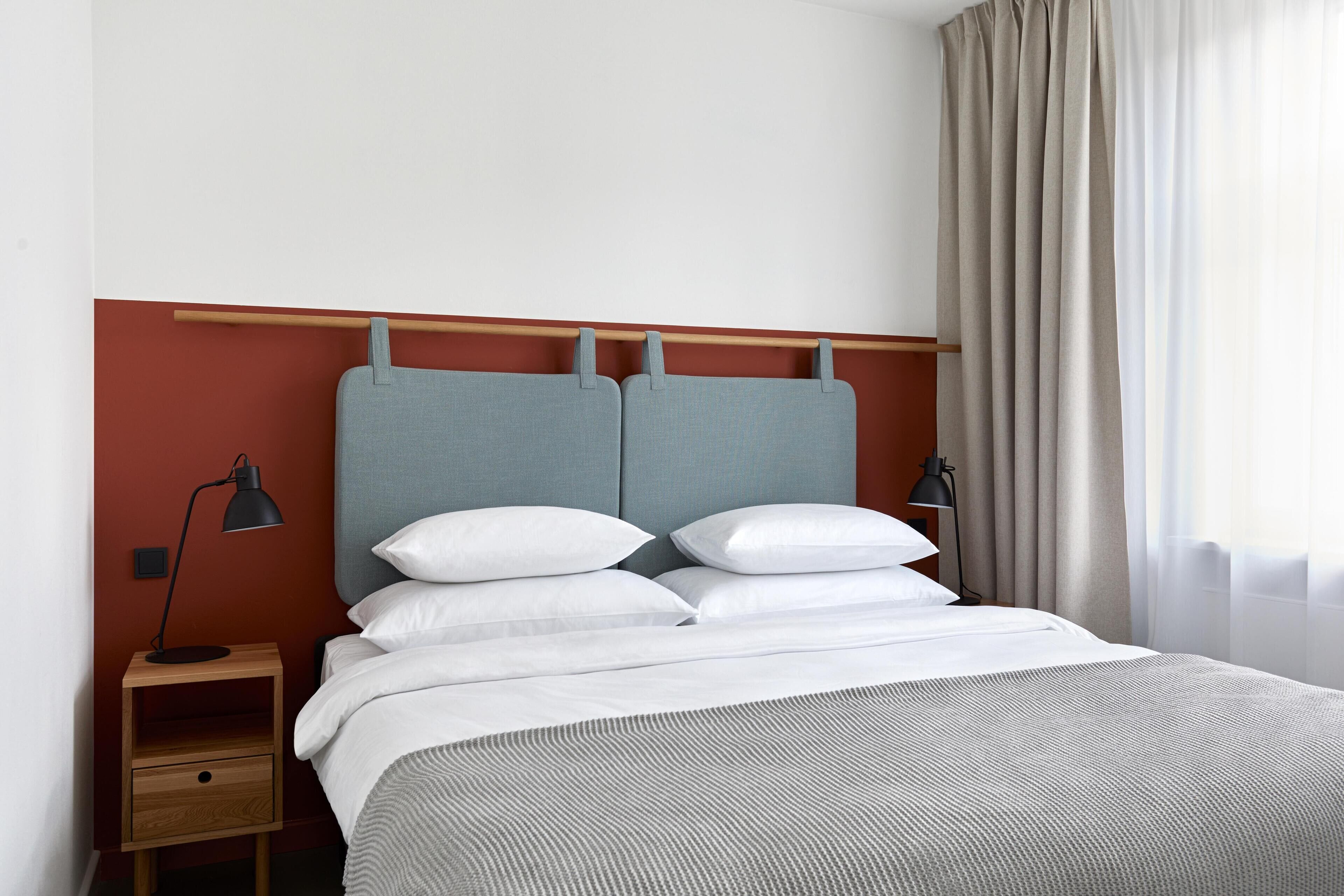A neatly made bed with a grey headboard, white bedding, and a wooden nightstand with a lamp.