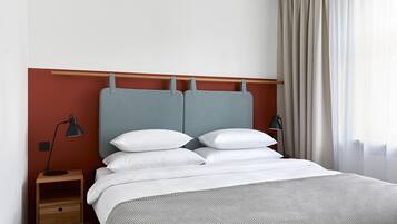 Un lit bien fait, avec une tête de lit grise, du linge de lit blanc et une table de chevet en bois surmontée d’une lampe.