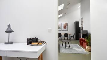 Een moderne woonruimte met een wit bureau, een camera en boeken, die uitkomt op een eethoek met stoelen en een tafel.