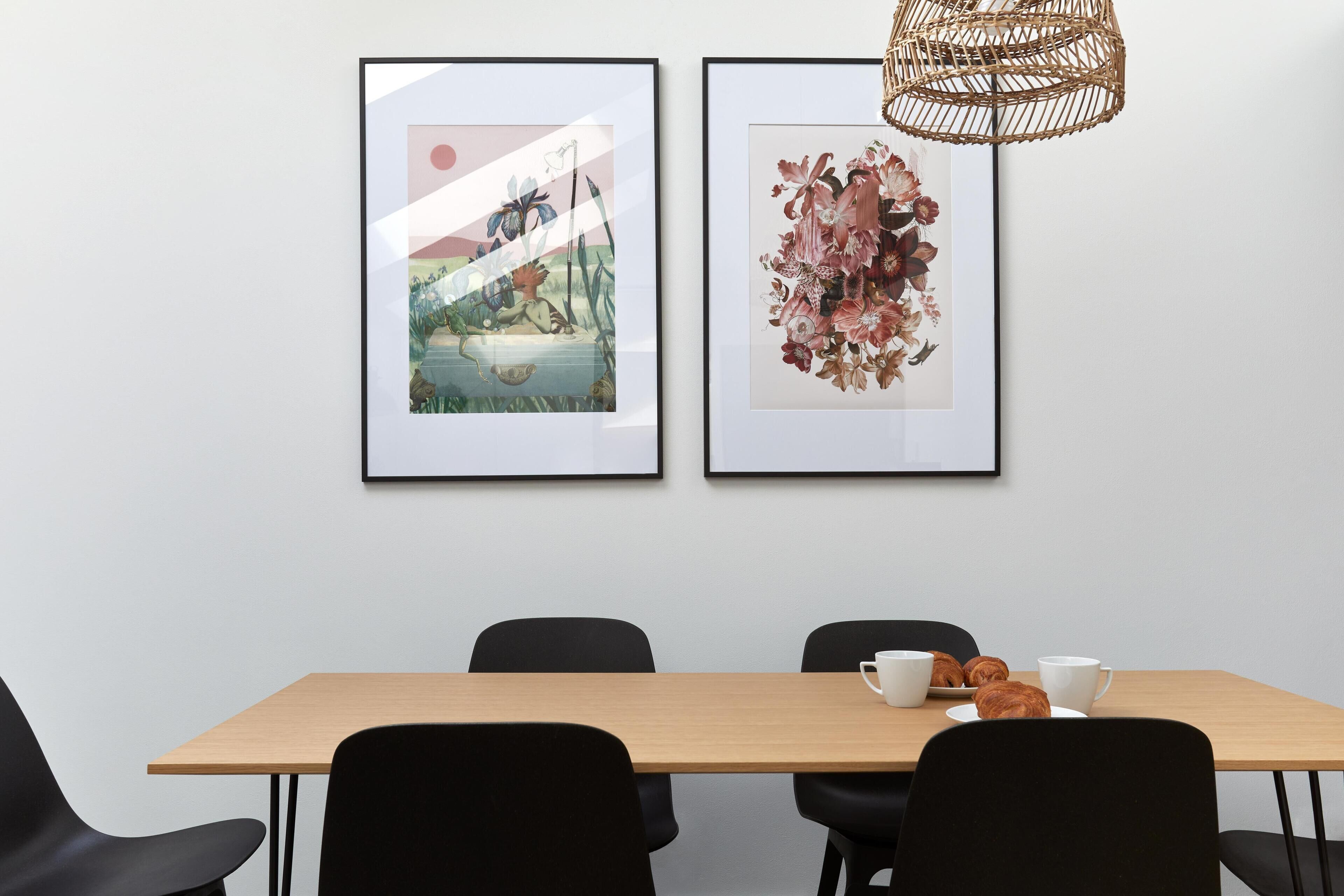Ein Konferenzraum mit einem Holztisch, schwarzen Stühlen und zwei gerahmten Kunstwerken an der Wand.