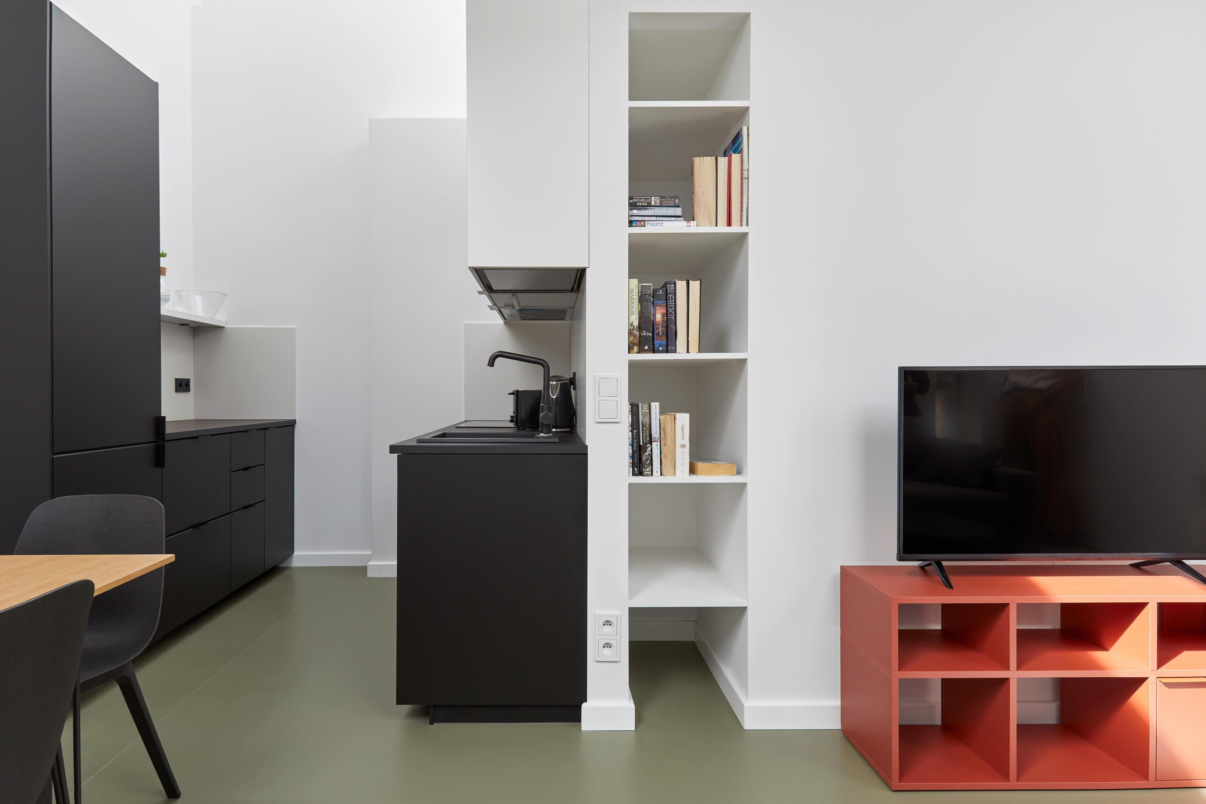 Un espace de vie moderne comprenant un coin cuisine, une bibliothèque, un téléviseur et un meuble de rangement rouge.