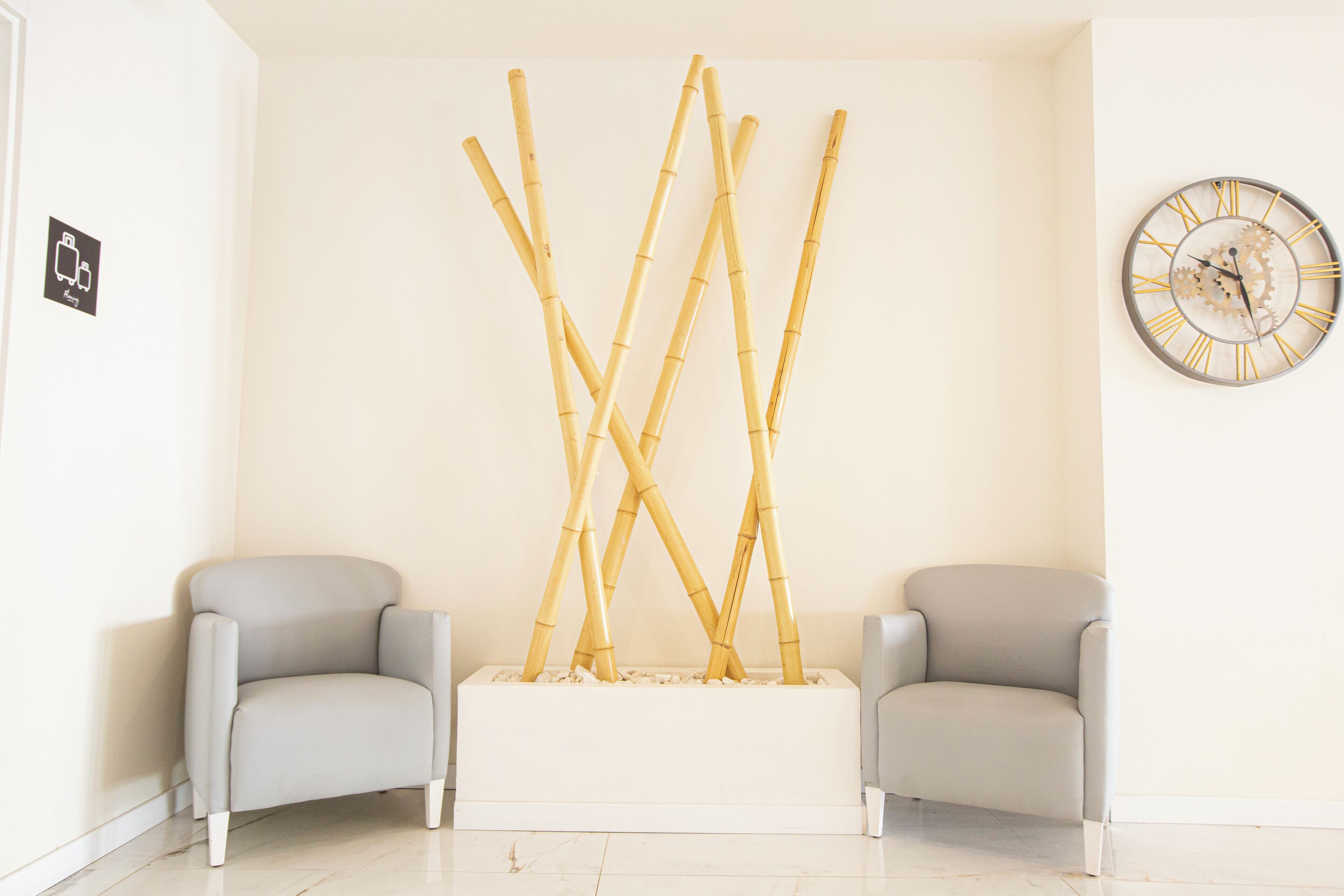 Una habitación con dos sillones grises, suelo blanco, un reloj de pared y una escultura de bambú.