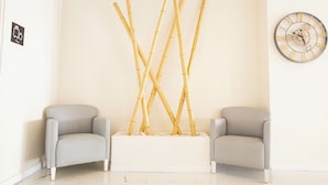 A room with two grey armchairs, a white floor, a wall-mounted clock, and a bamboo sculpture. - Hotel Fleming Playa Poniente (Benidorm)