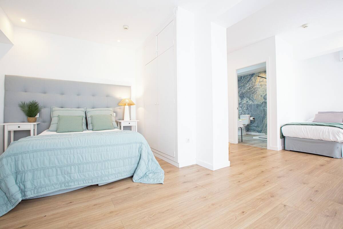 A modern bedroom with a large bed, bedside tables, a nightstand, and a view of a bathroom.