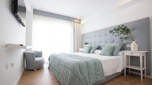A modern bedroom with a large bed, a grey upholstered headboard, a bedside table with a lamp, and a small grey armchair. - Hotel Fleming Playa Poniente (Benidorm)