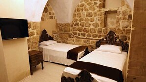 A room with two beds, a TV, and stone walls.