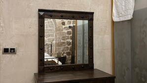 A room with a wooden desk, a mirror with lights, a stone wall, and a patterned wallpaper.