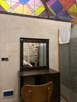 Una habitación con un escritorio de madera, un espejo con luces, una pared de piedra y un papel tapiz estampado.