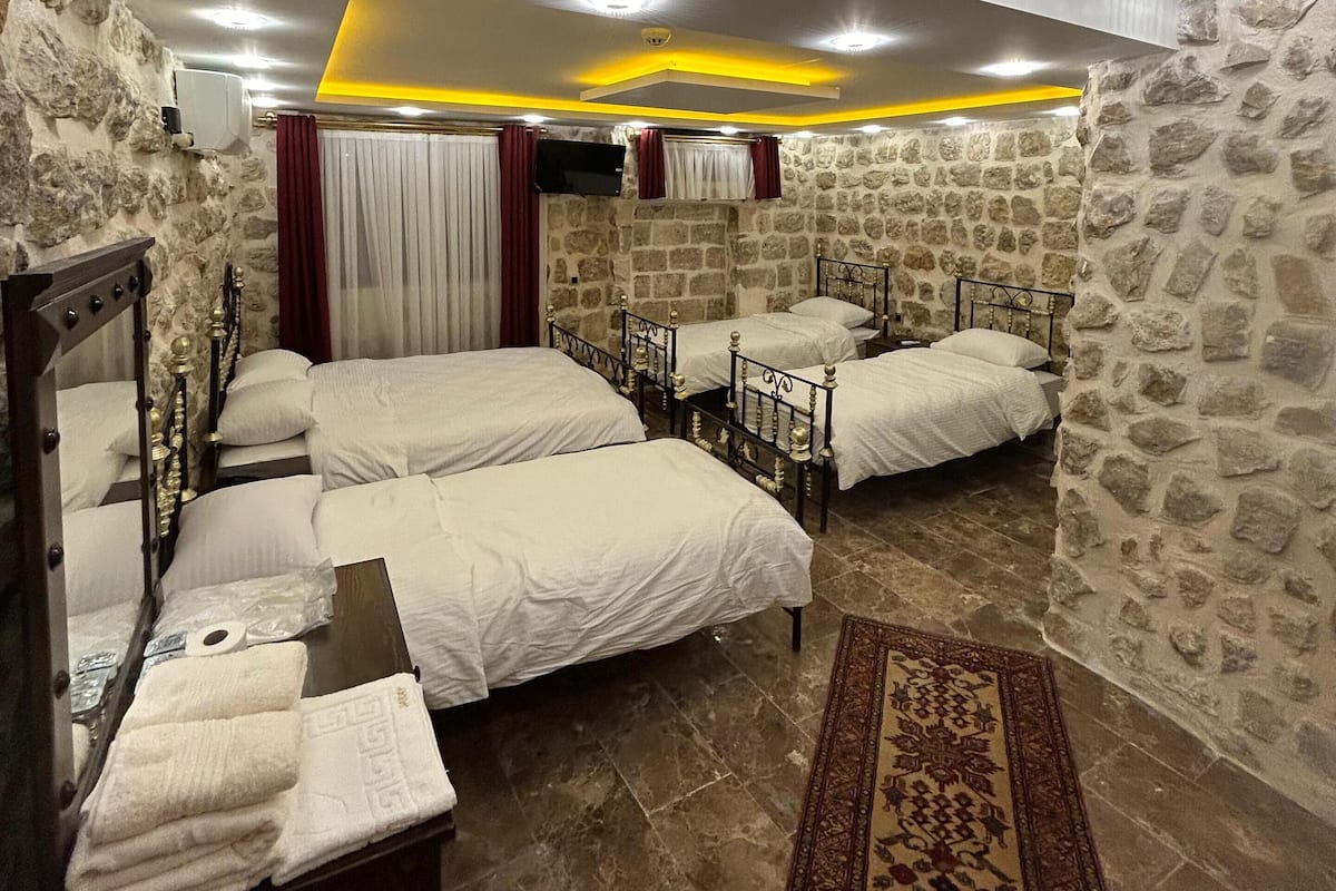 Habitación de hotel con cuatro camas, paredes de piedra y un diseño moderno en el techo.