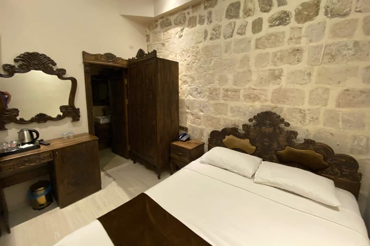 Ein Schlafzimmer mit Steinwand, einem hölzernen Bett mit weißer Bettwäsche, einem Holzschrank und einem Spiegel.