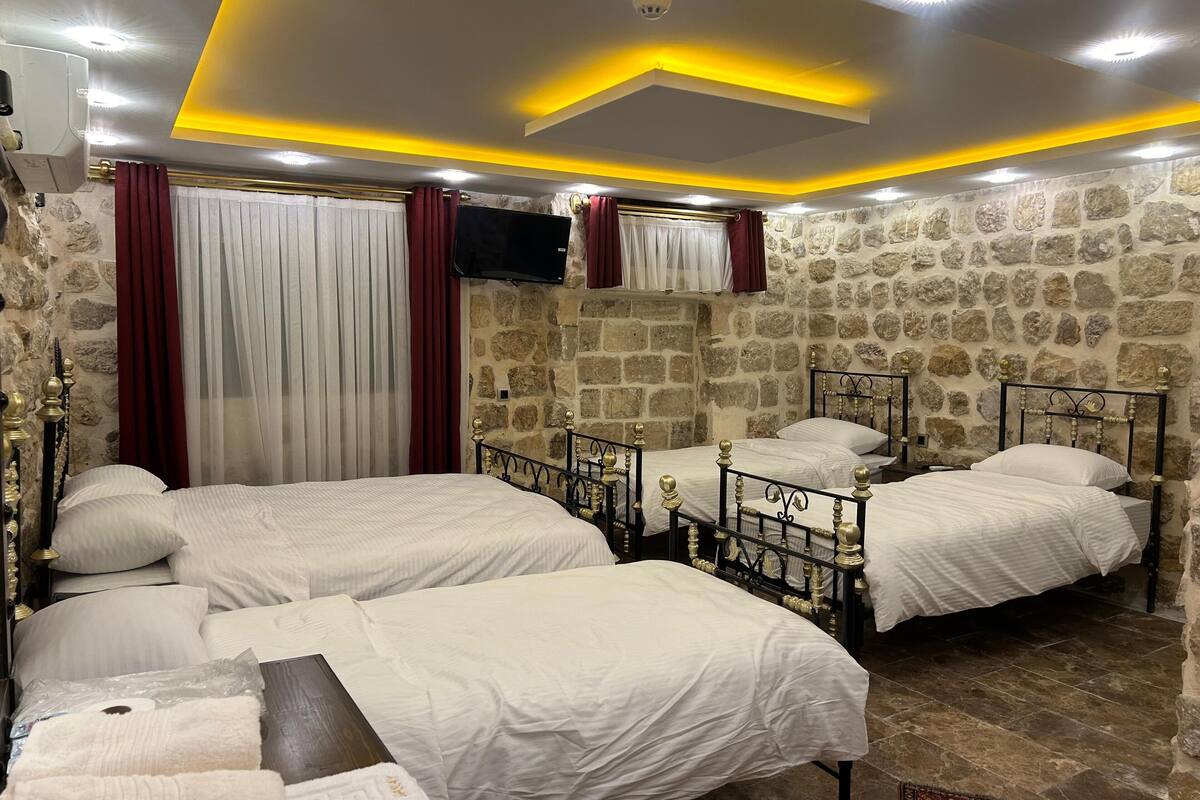 Ein Hotelzimmer mit drei Betten, Steinwänden und einem modernen Deckenstil.