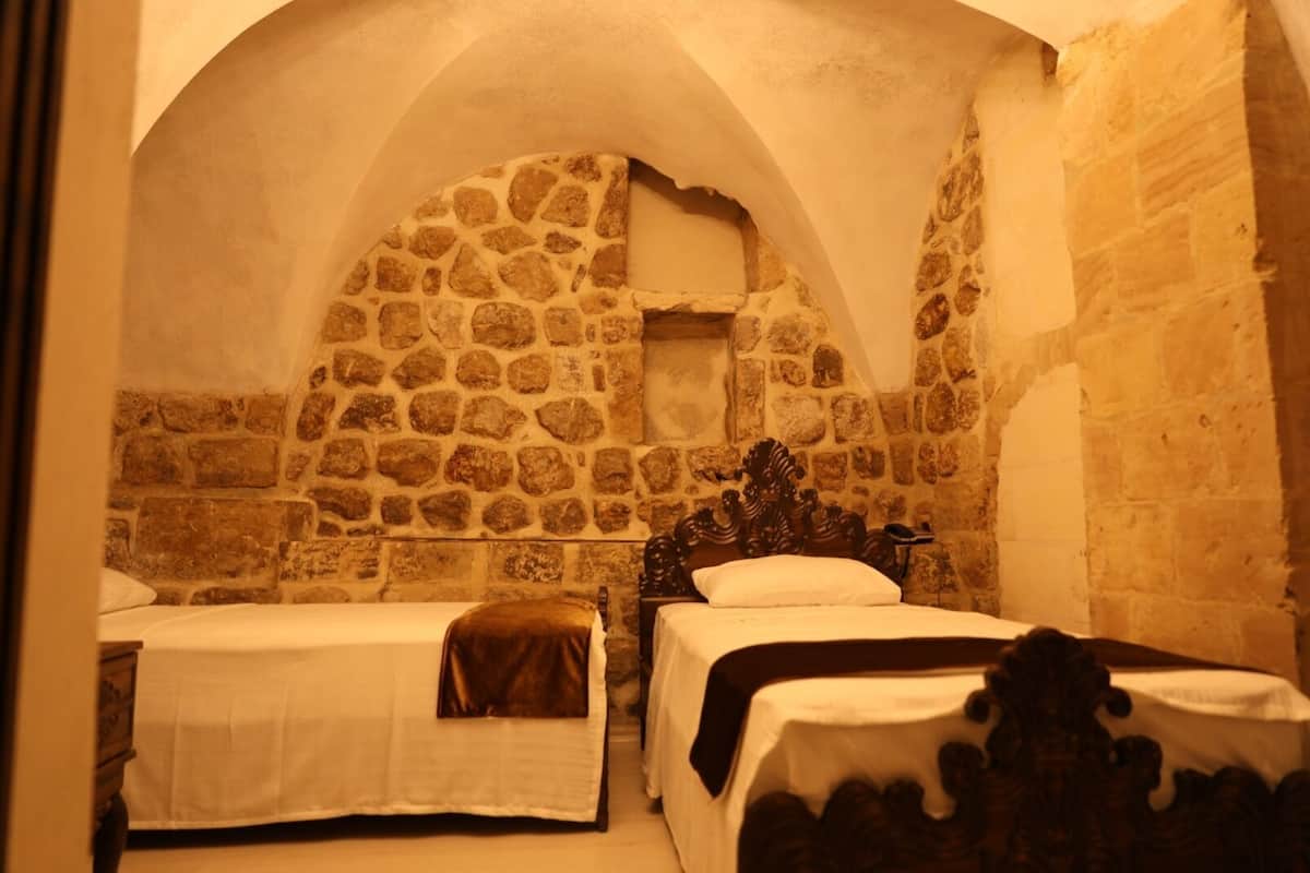 Ein Zimmer mit zwei Betten, Steinwänden und einer gewölbten Decke.