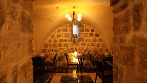 A stone-walled dining area with a chandelier, marble flooring, and tables and chairs.