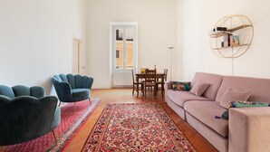 Ein Wohnzimmer mit einer Couch, zwei Sesseln, einem Esstisch und einem gemusterten Teppich.