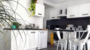 Een moderne keuken met witte kastjes, een vaatwasser, een koffiezetapparaat en een eethoek met witte stoelen.