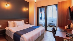 Habitación de hotel con una cama grande, un escritorio con una silla, un televisor y un ventanal corredero que da a un balcón.