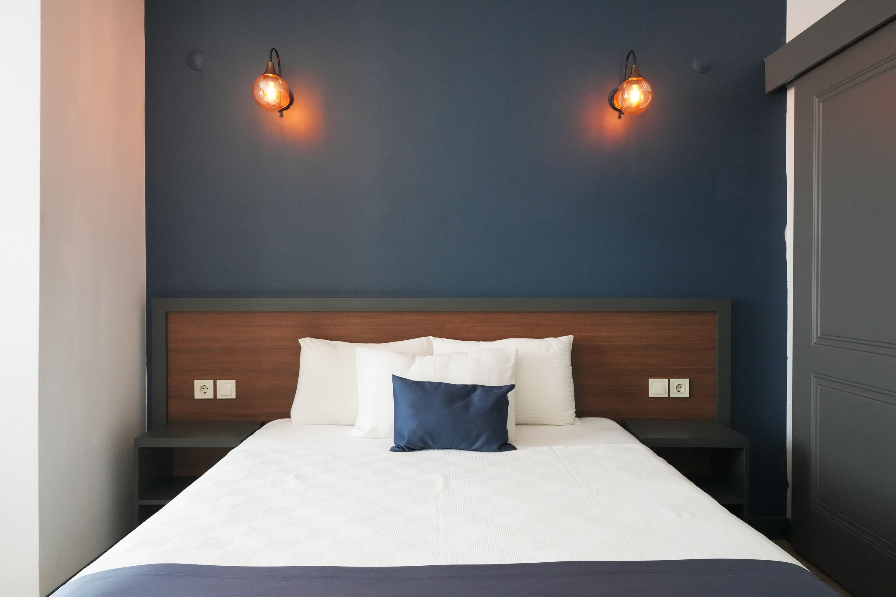 A hotel room with a bed, two bedside tables, and two wall-mounted lights.