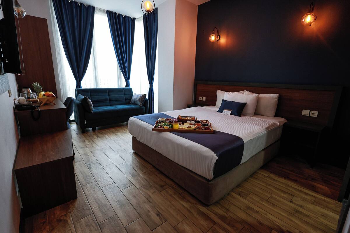 Habitación de hotel con una cama grande, una mesita de noche, un escritorio, una silla y una ventana con cortinas.