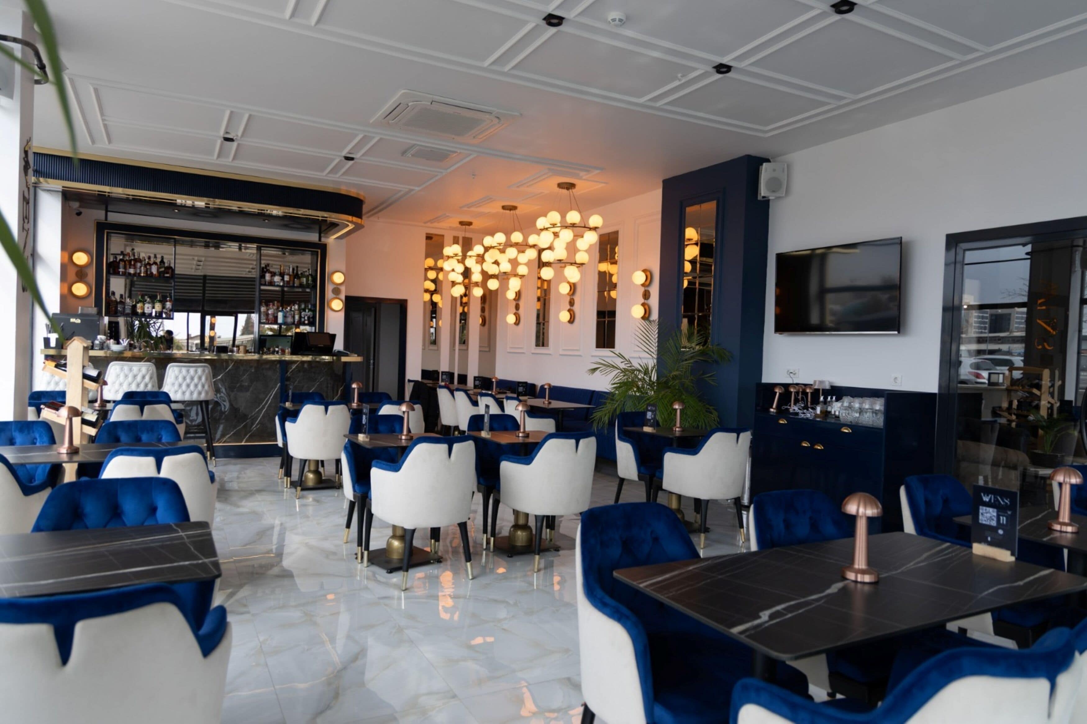 A modern restaurant interior with a bar area, white and blue upholstered chairs, and a marble floor.