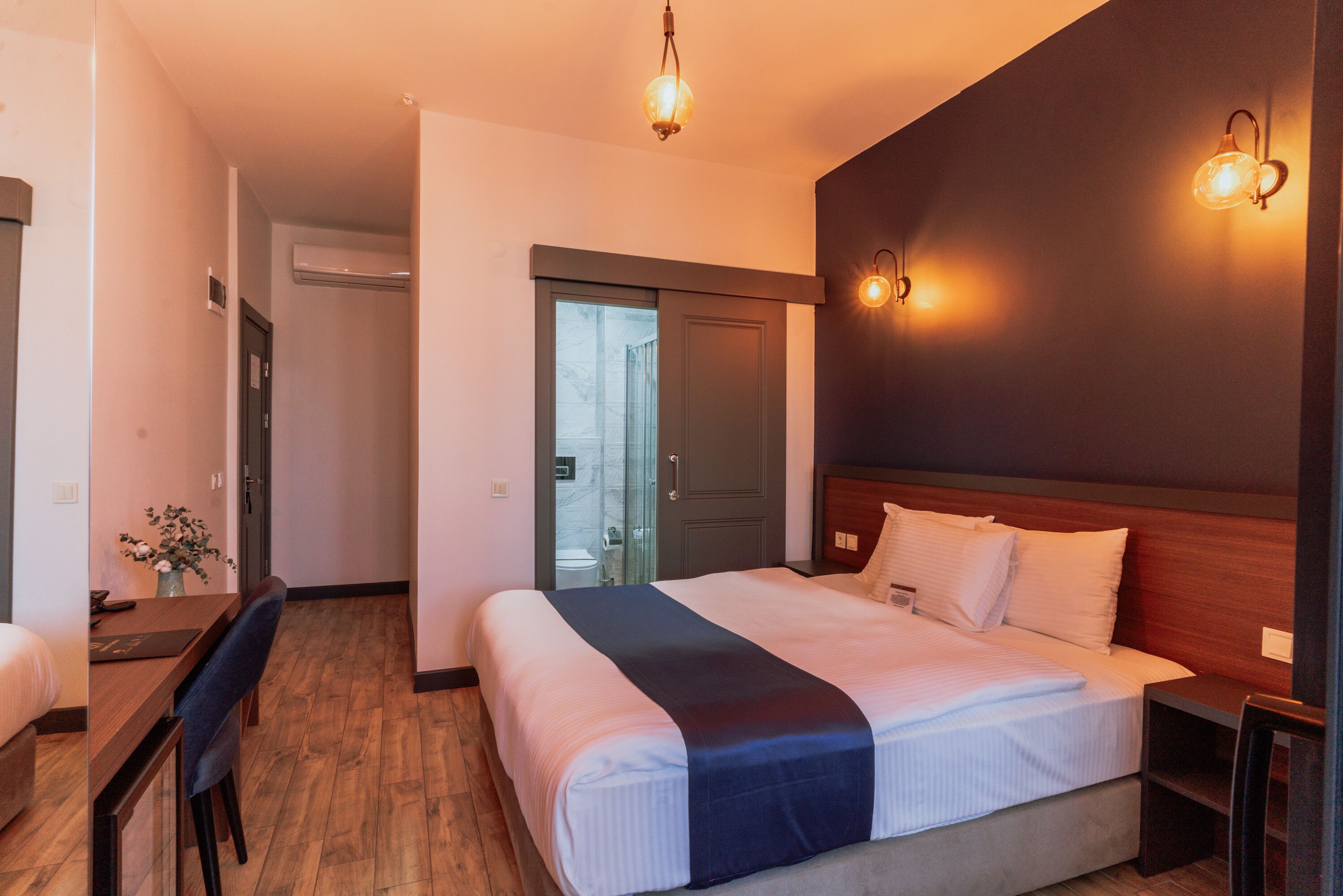 A hotel room with a large bed, a desk, and a chair. There is a door leading to a bathroom and a hallway.