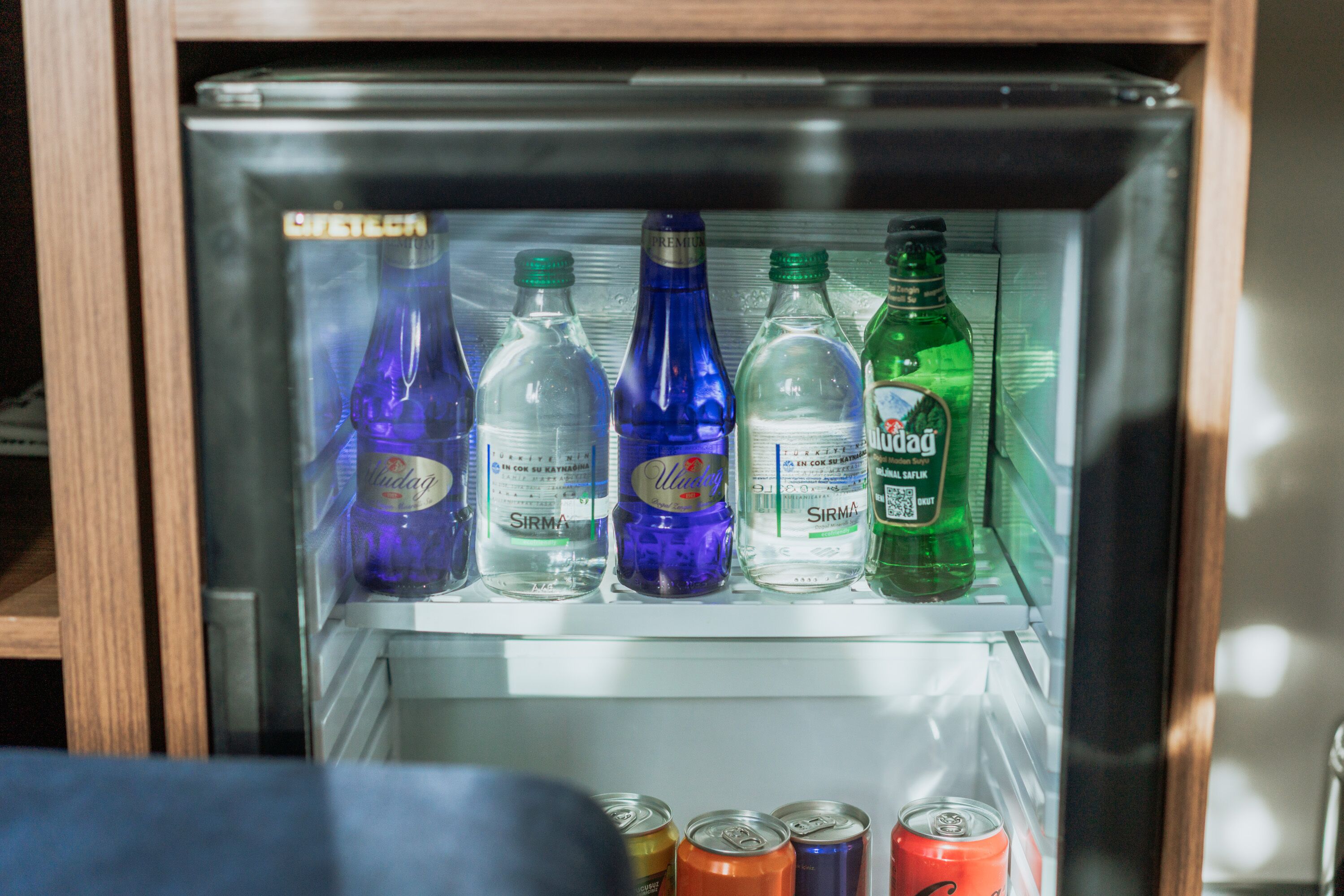 Un refrigerador lleno de diversas bebidas, incluyendo botellas y latas.