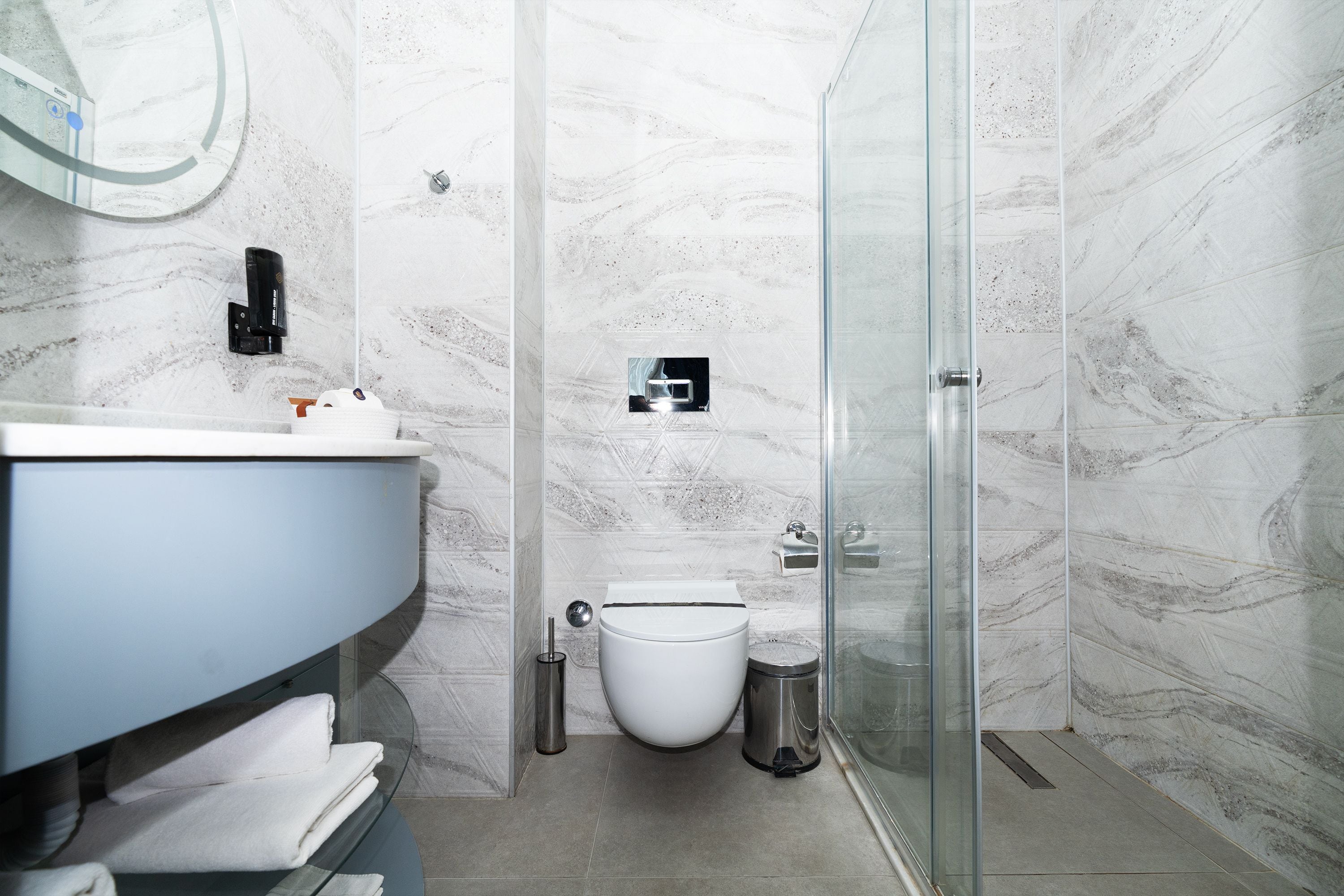 Een moderne badkamer met een douchecabine van glas, een wit toilet en een wastafel met zeepdispenser.