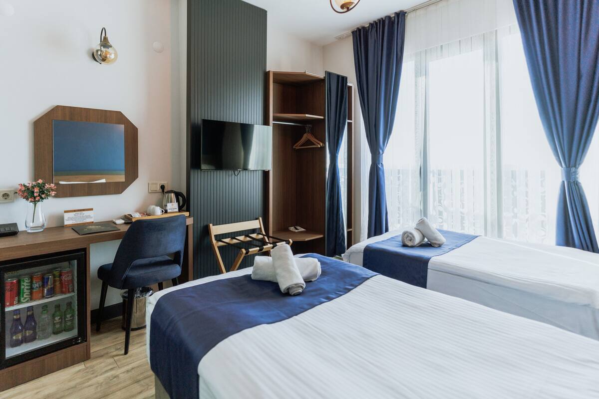 Habitación de hotel con dos camas, un escritorio con computadora, televisión, armario y minibar.