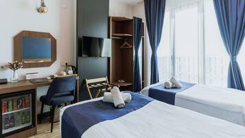 A hotel room with two beds, a desk with a computer, a TV, a wardrobe, and a minibar.