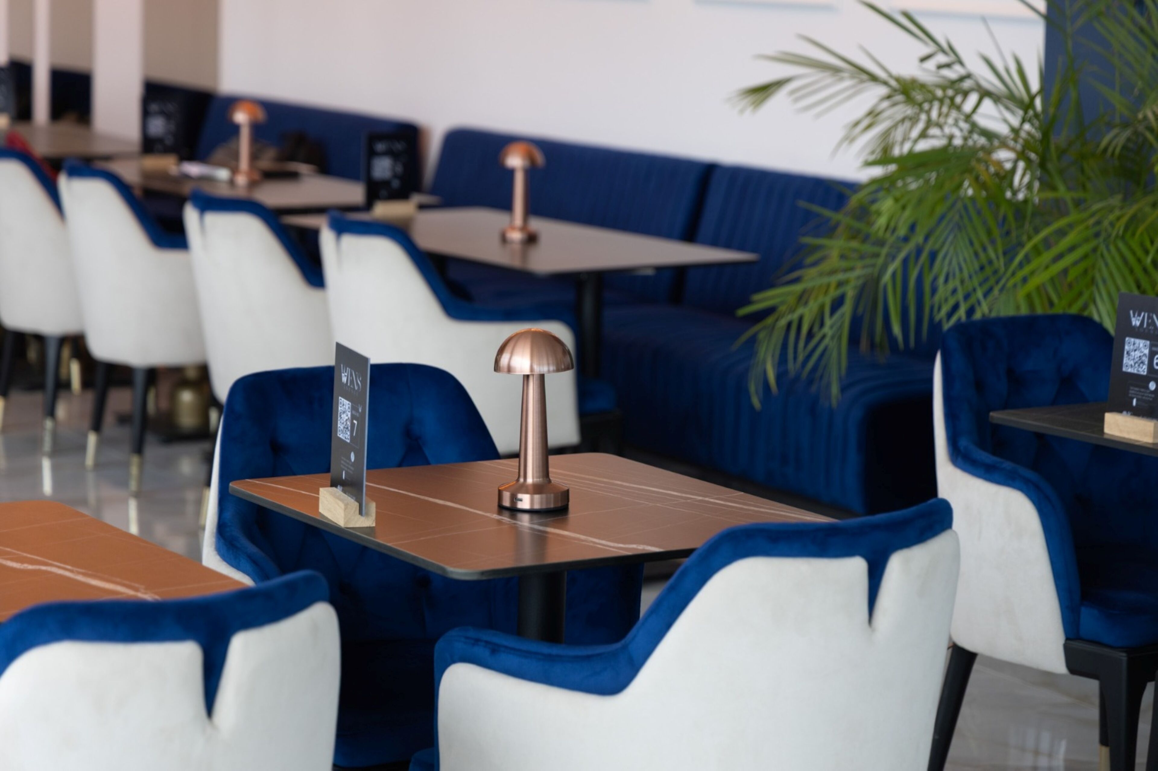 Un restaurante moderno con asientos azules y blancos, una lámpara de cobre y un código QR en la mesa.